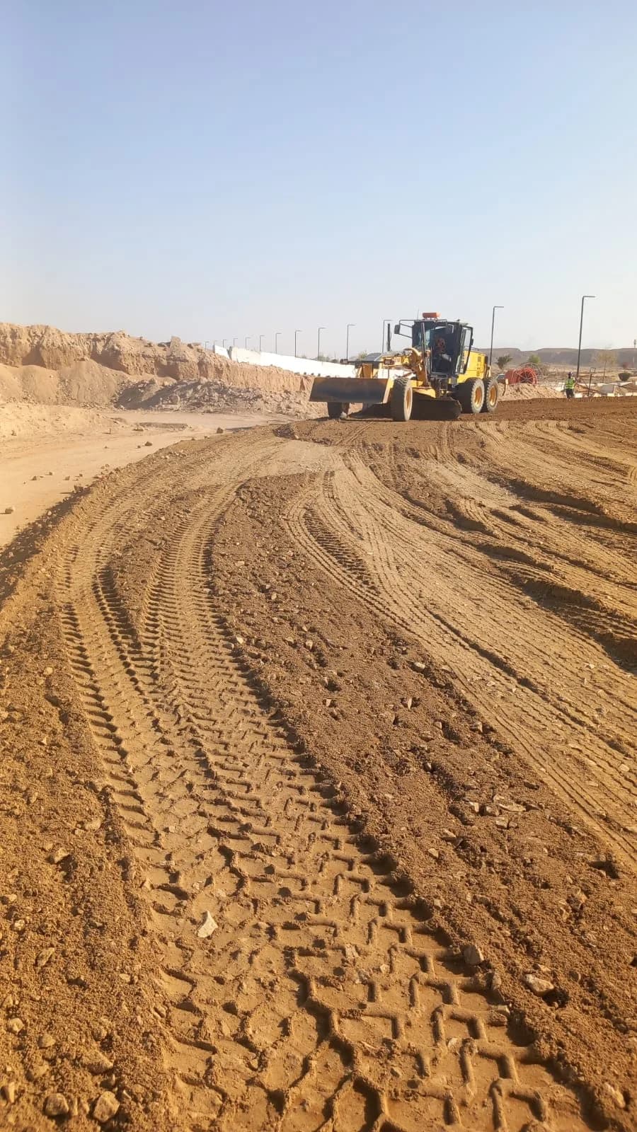 Motor grader preparing earthworks and road base in a desert construction corridor.