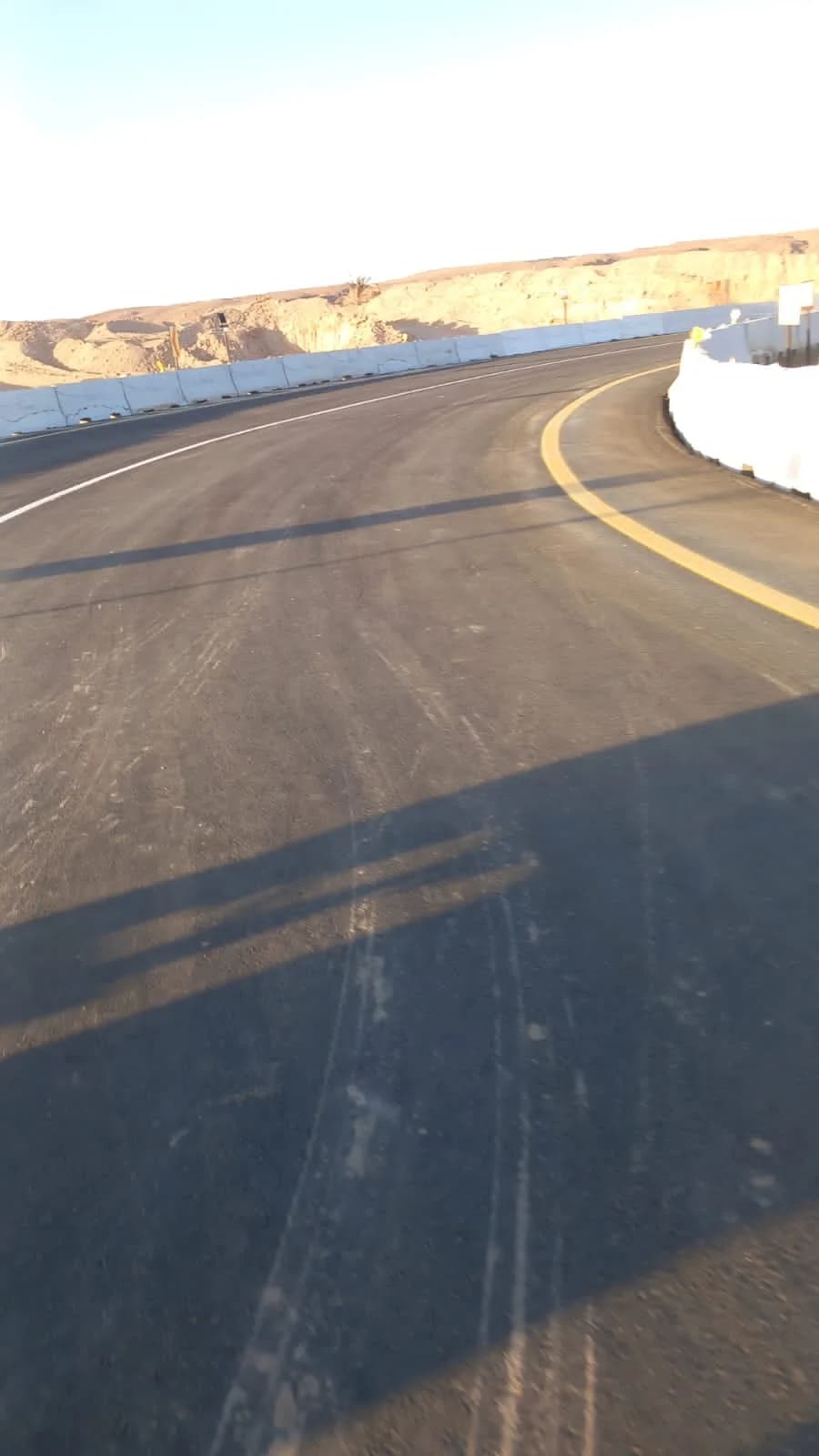 Curved asphalt road surface with lane markings and concrete barriers in a desert project area.