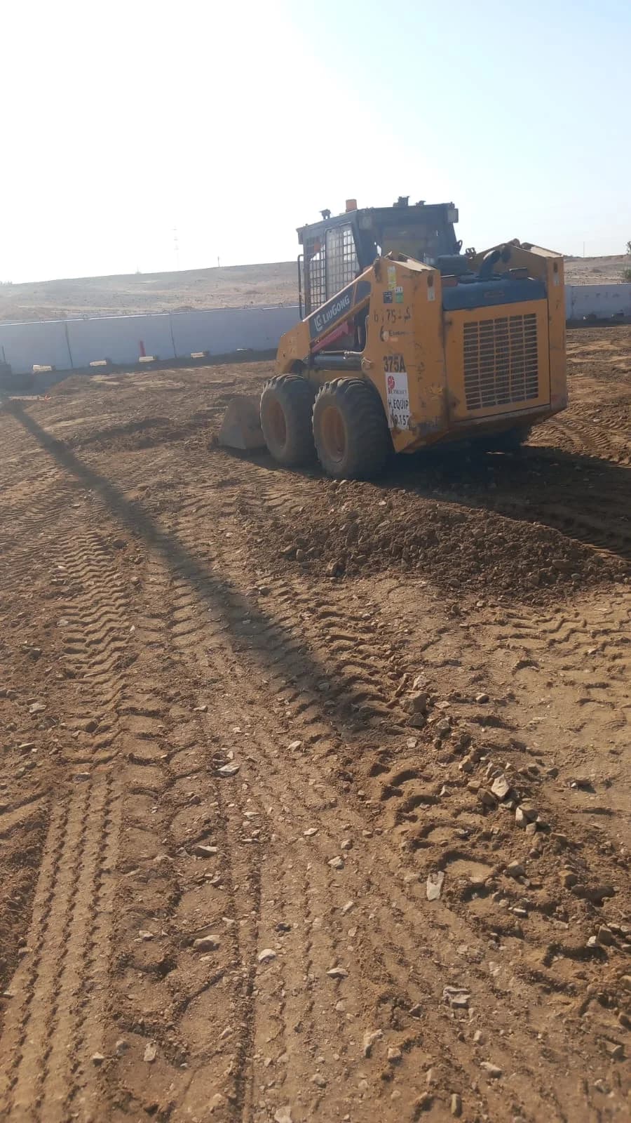 Skid loader preparing rough ground and road base material.